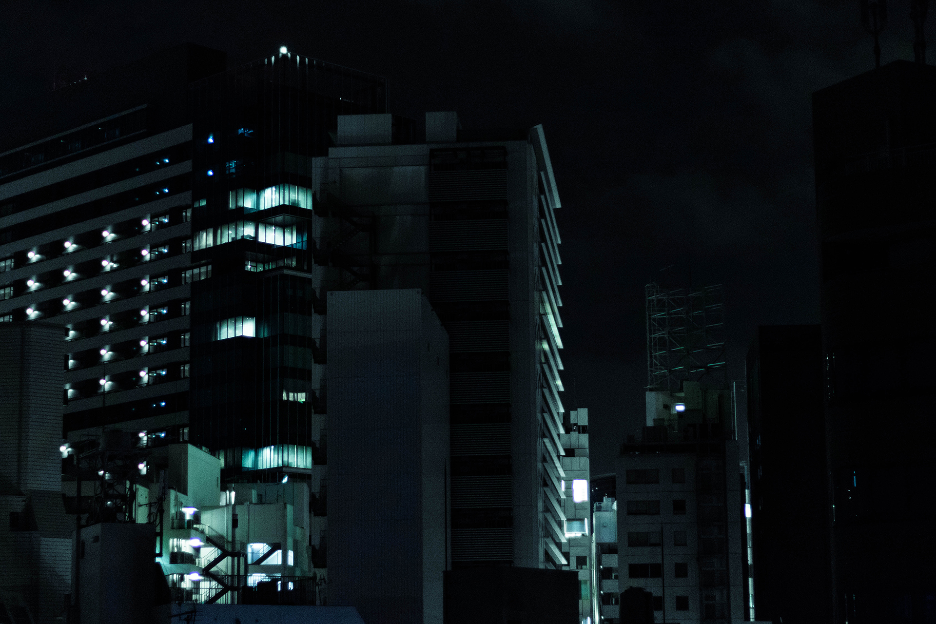 Dark towering modern cluster of buildings dimly illuminated by their windwos.